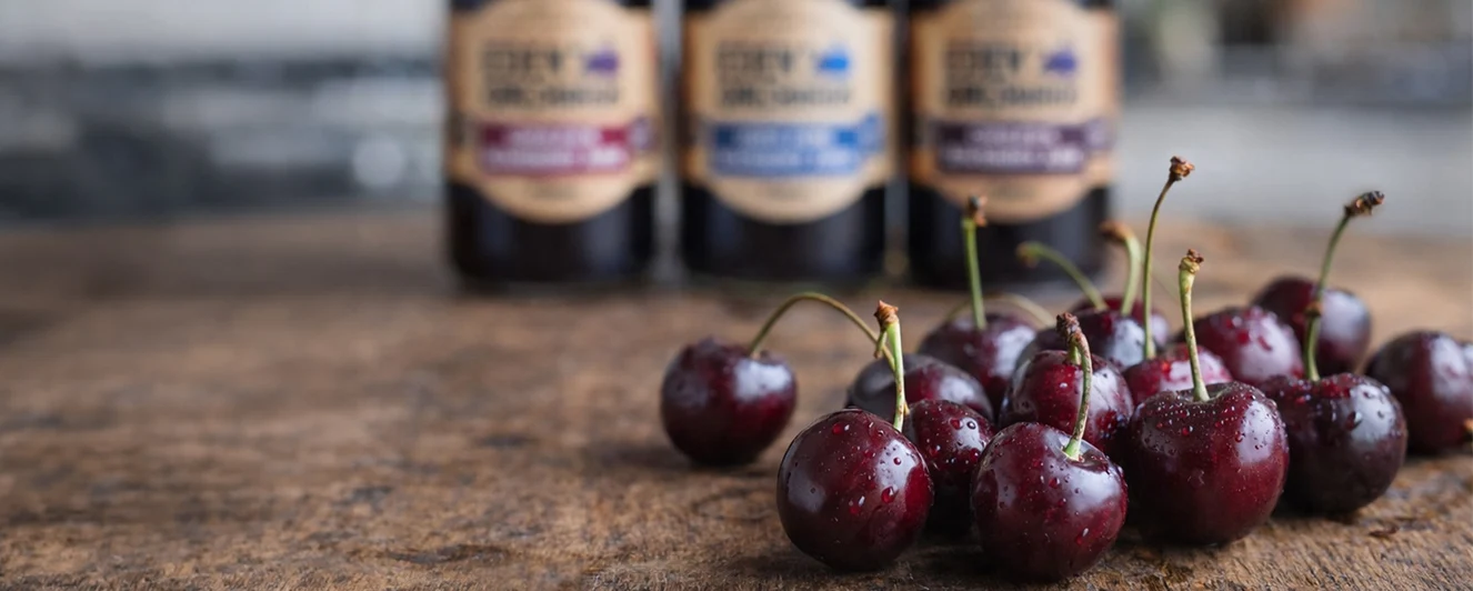 Fresh cherries on a wooden bench with Eden Orchards bottles behind