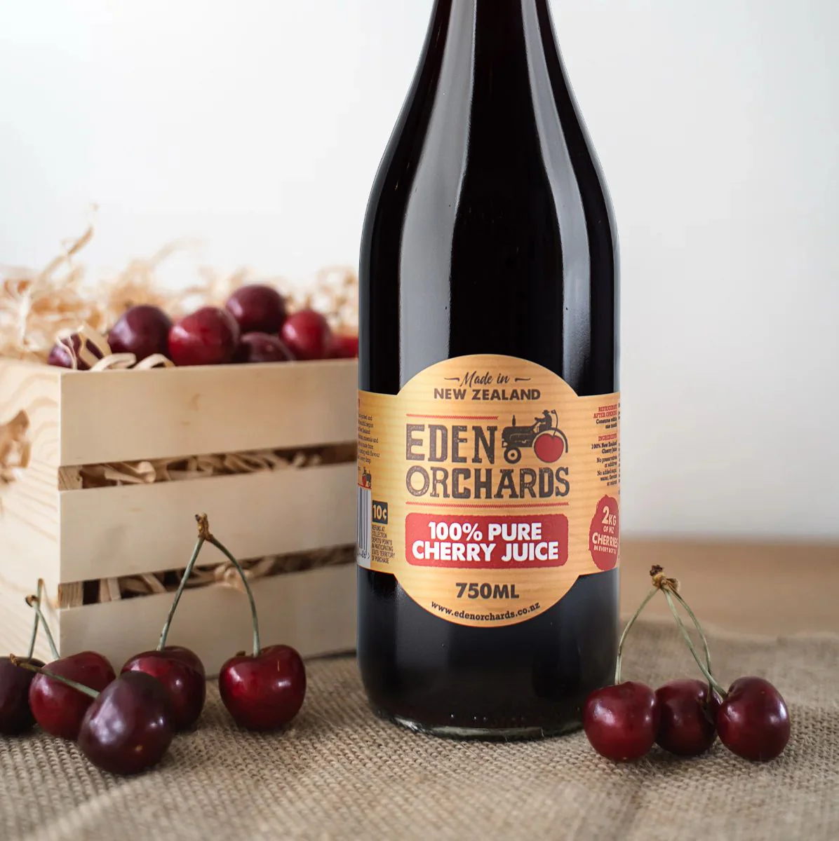 A 750ml bottle of Eden Orchards Pure Cherry Juice beside a crate of Central Otago cherries